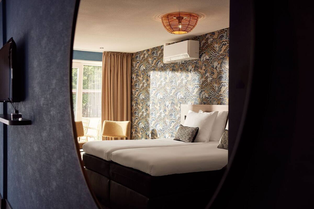 A hotel room with a bed, two chairs, a TV, and a window with curtains.