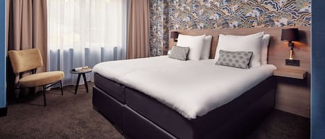 Una habitación de hotel con una cama grande, una silla, una mesita y un papel tapiz estampado.