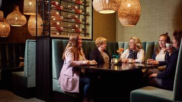 A group of people seated around a table in a cozy, dimly lit room with wicker pendant lights and a wine rack in the background.