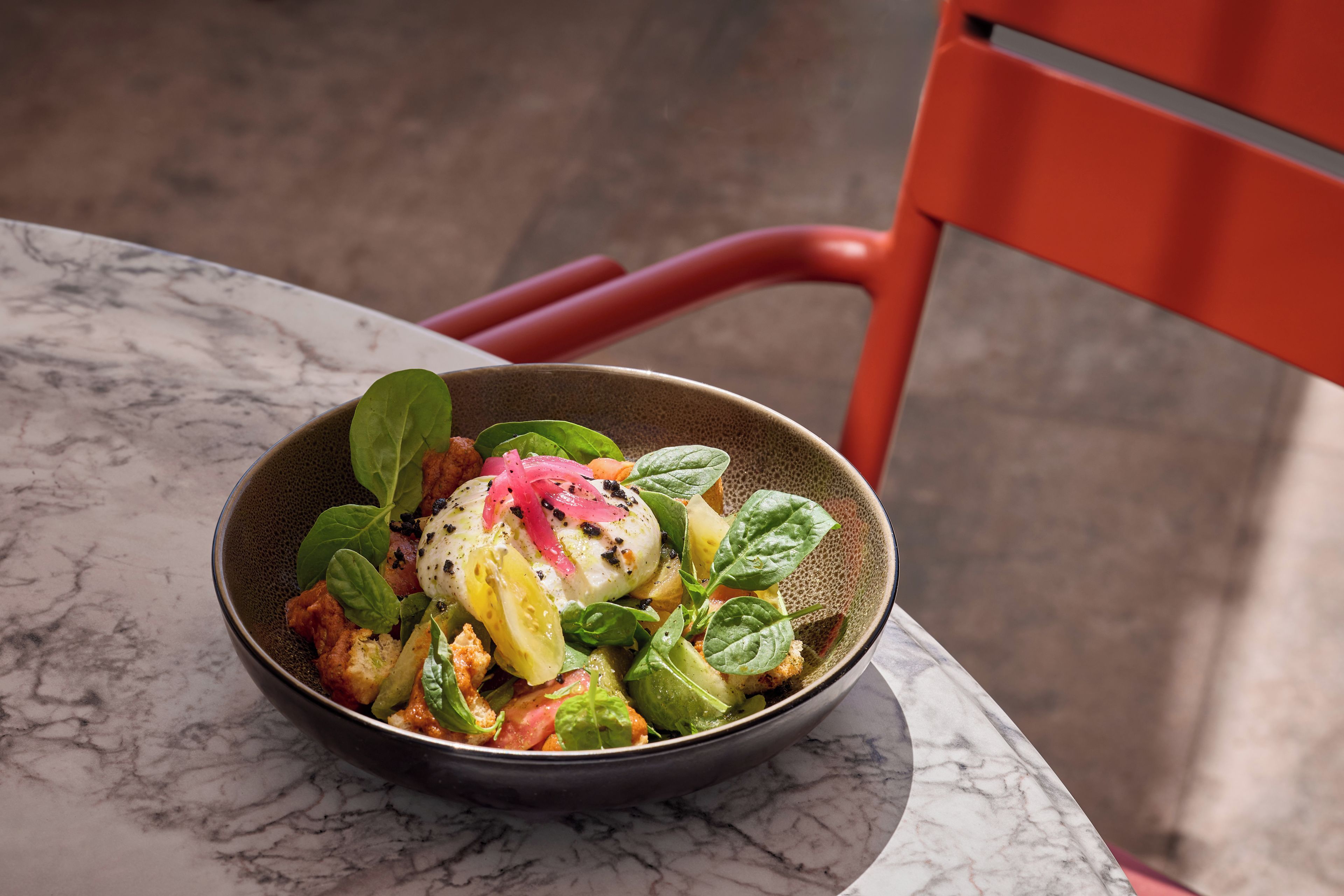 A bowl of food on a marble table with a red chair in the background.