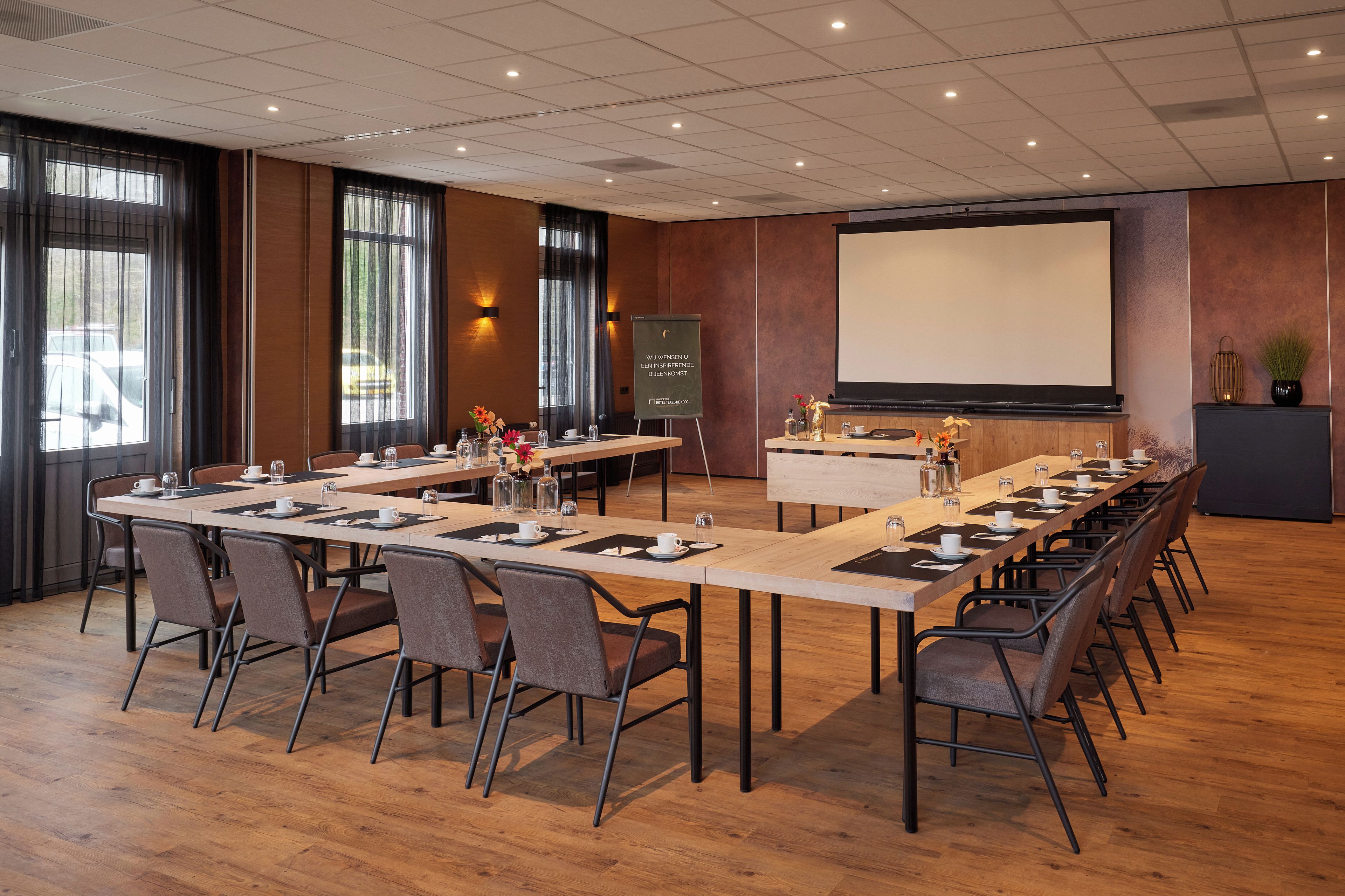 A conference room with a long table, chairs, a projector screen, and a presentation screen.
