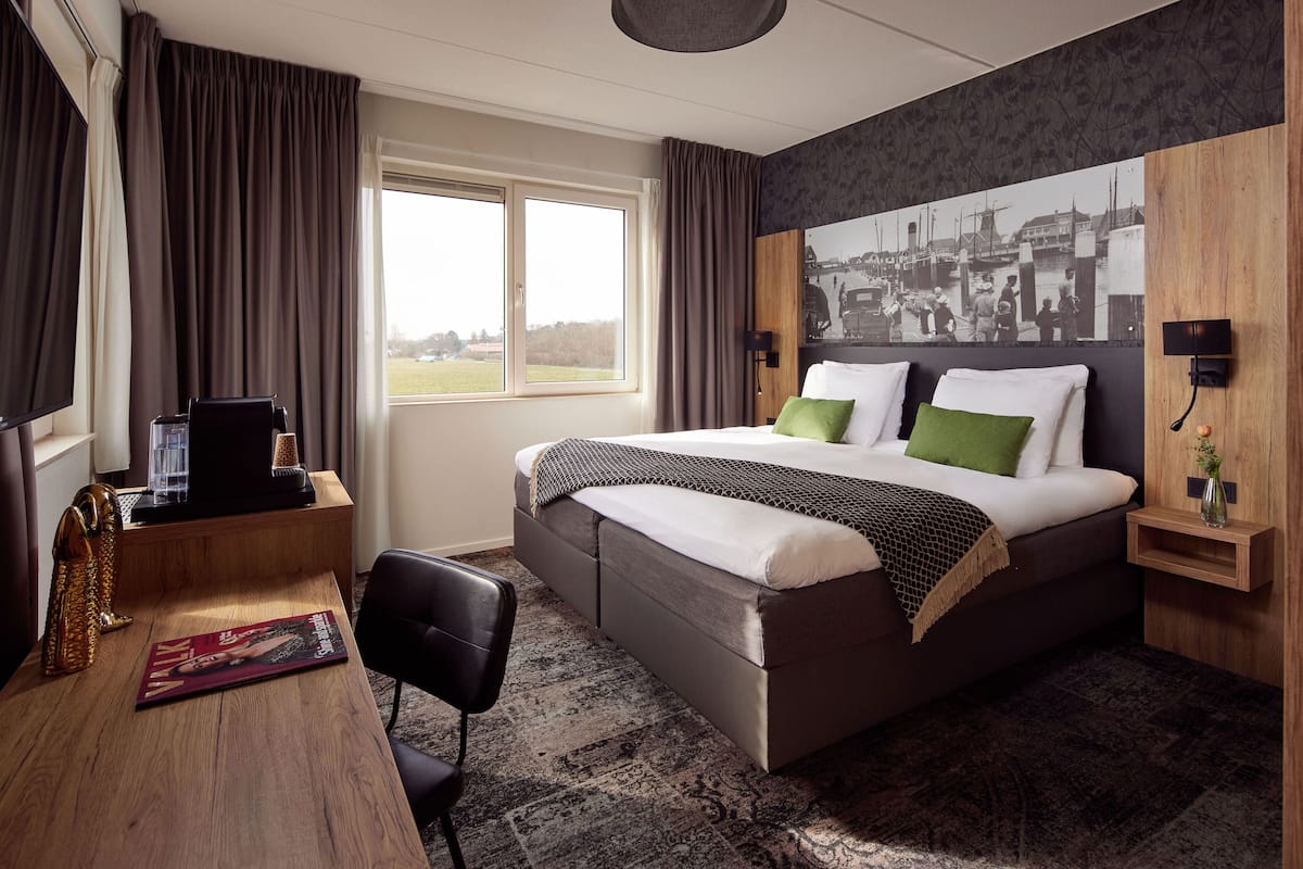 A hotel room with a large bed, a desk, a chair, a TV, and a window with curtains.