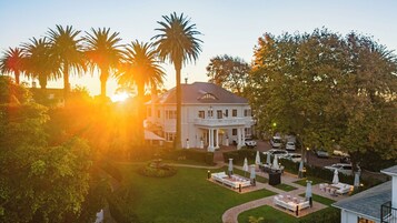A large white building with a balcony, surrounded by a well-maintained lawn and palm trees.