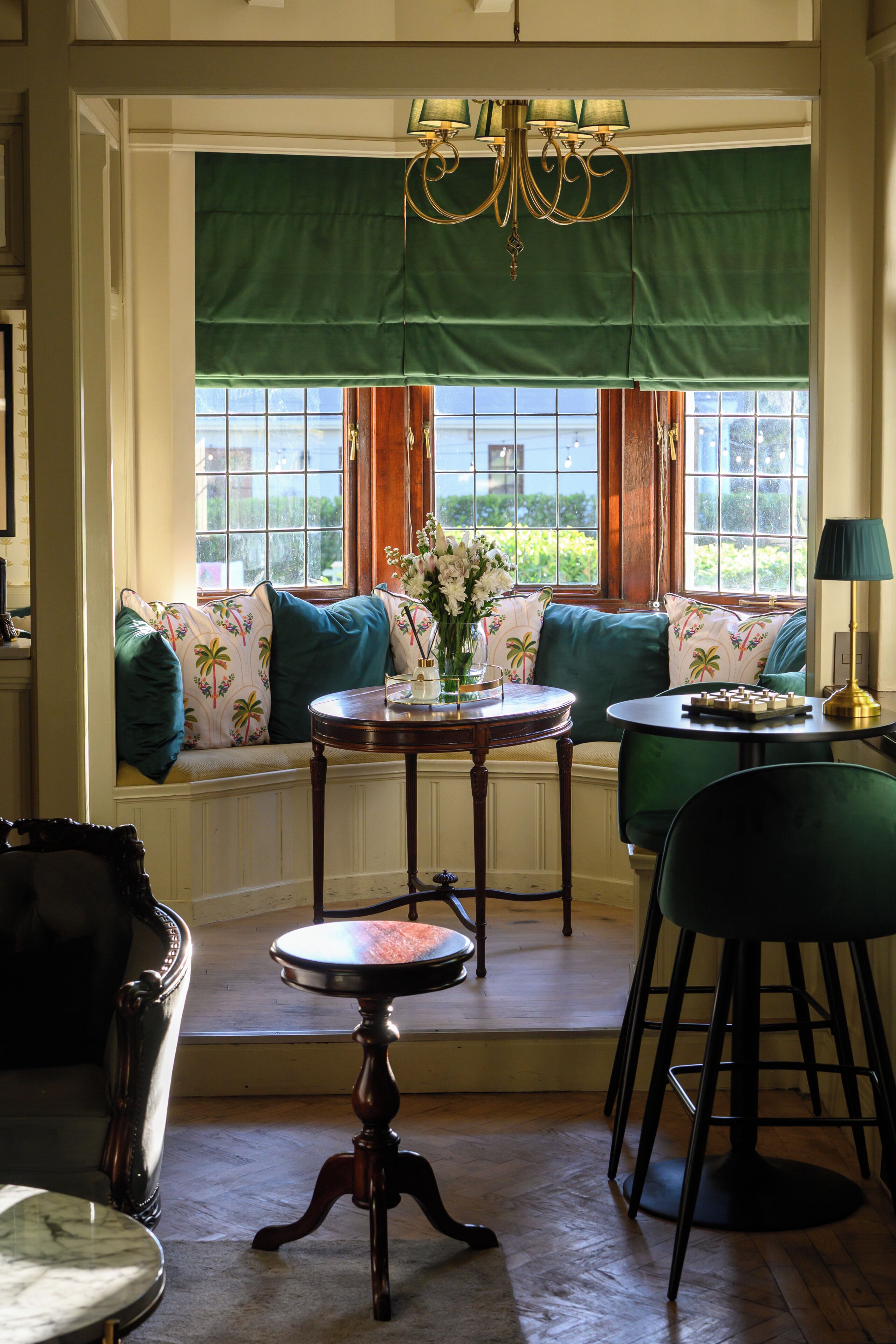 A room with a bay window, a table with a vase, a chair, and a lamp.