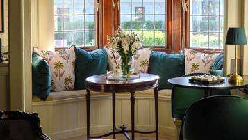A room with a bay window, a table with a vase, a chair, and a lamp.