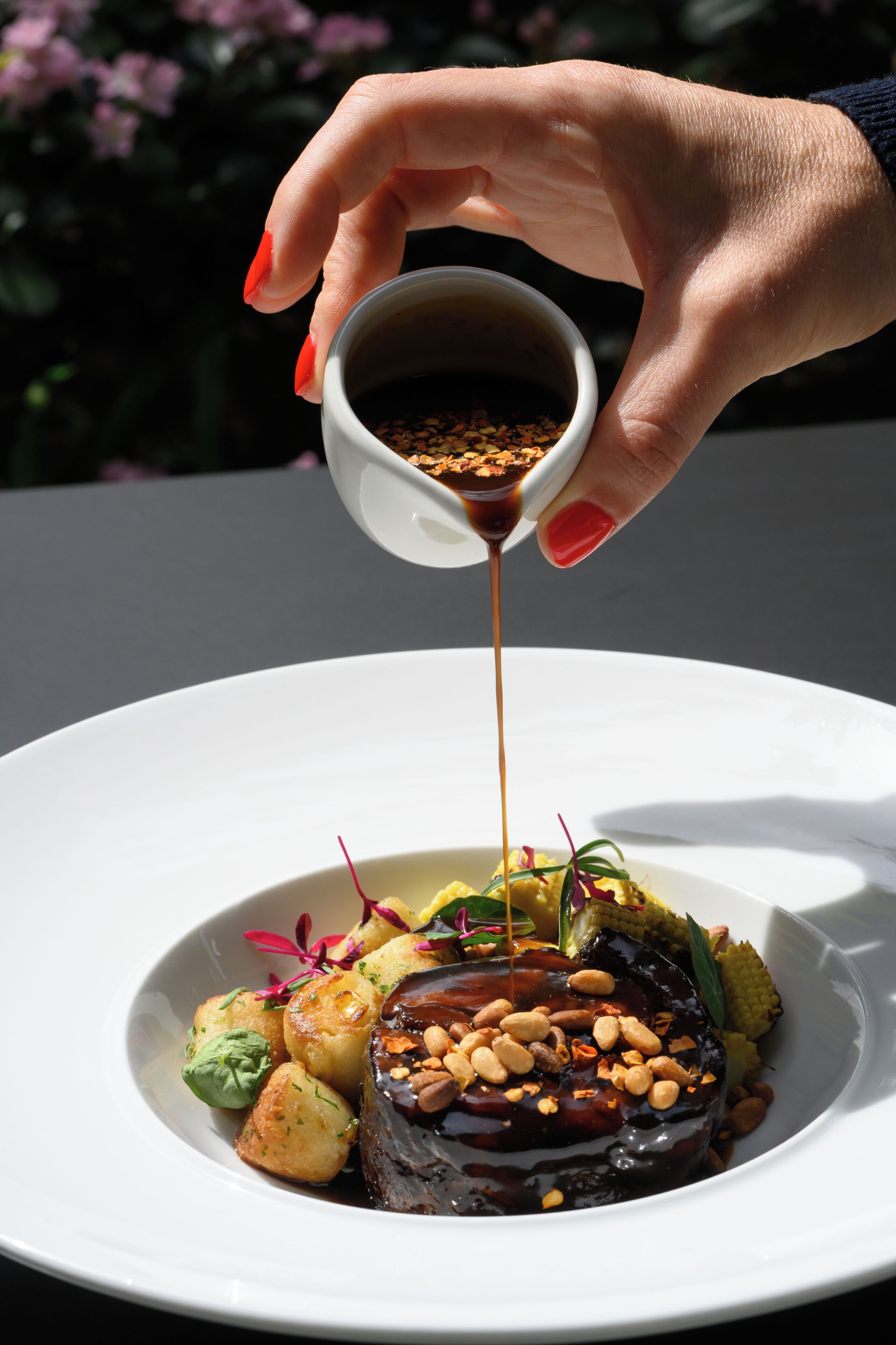 A hand pouring sauce over a dish on a white plate.