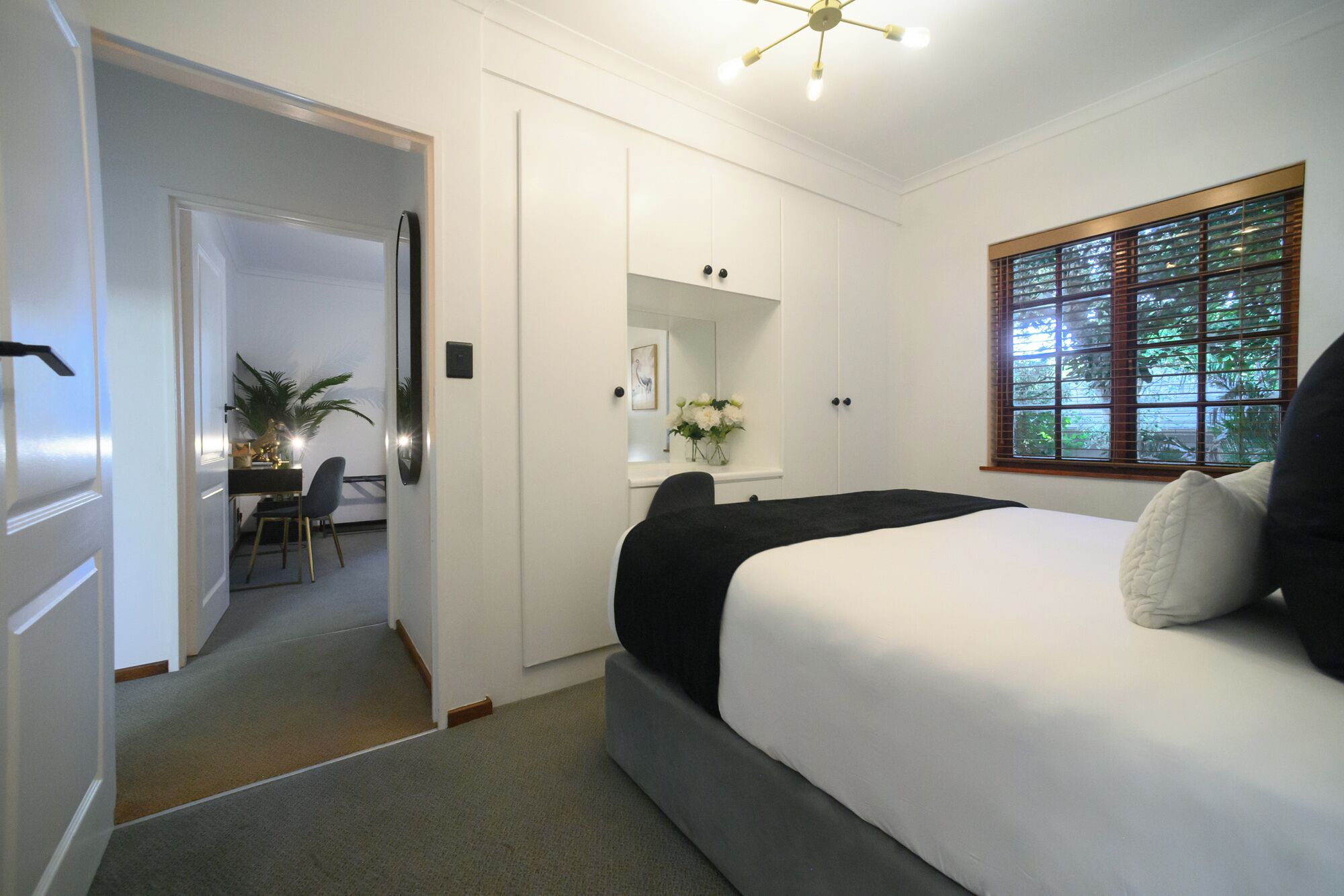Un dormitorio con cama, escritorio, silla, espejo y ventana con persianas.