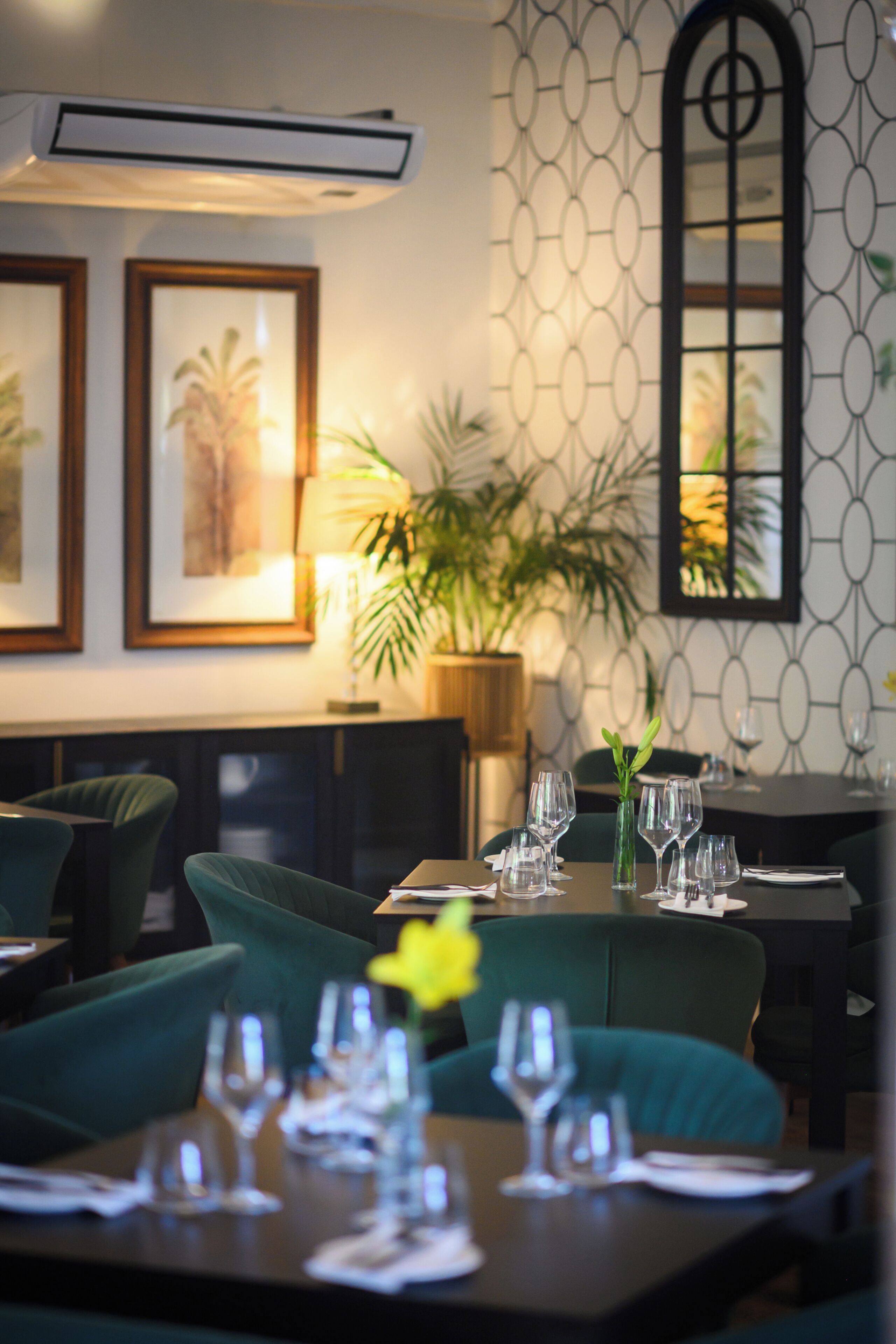 A restaurant with tables set for dining, framed artwork on the wall, and a potted plant.
