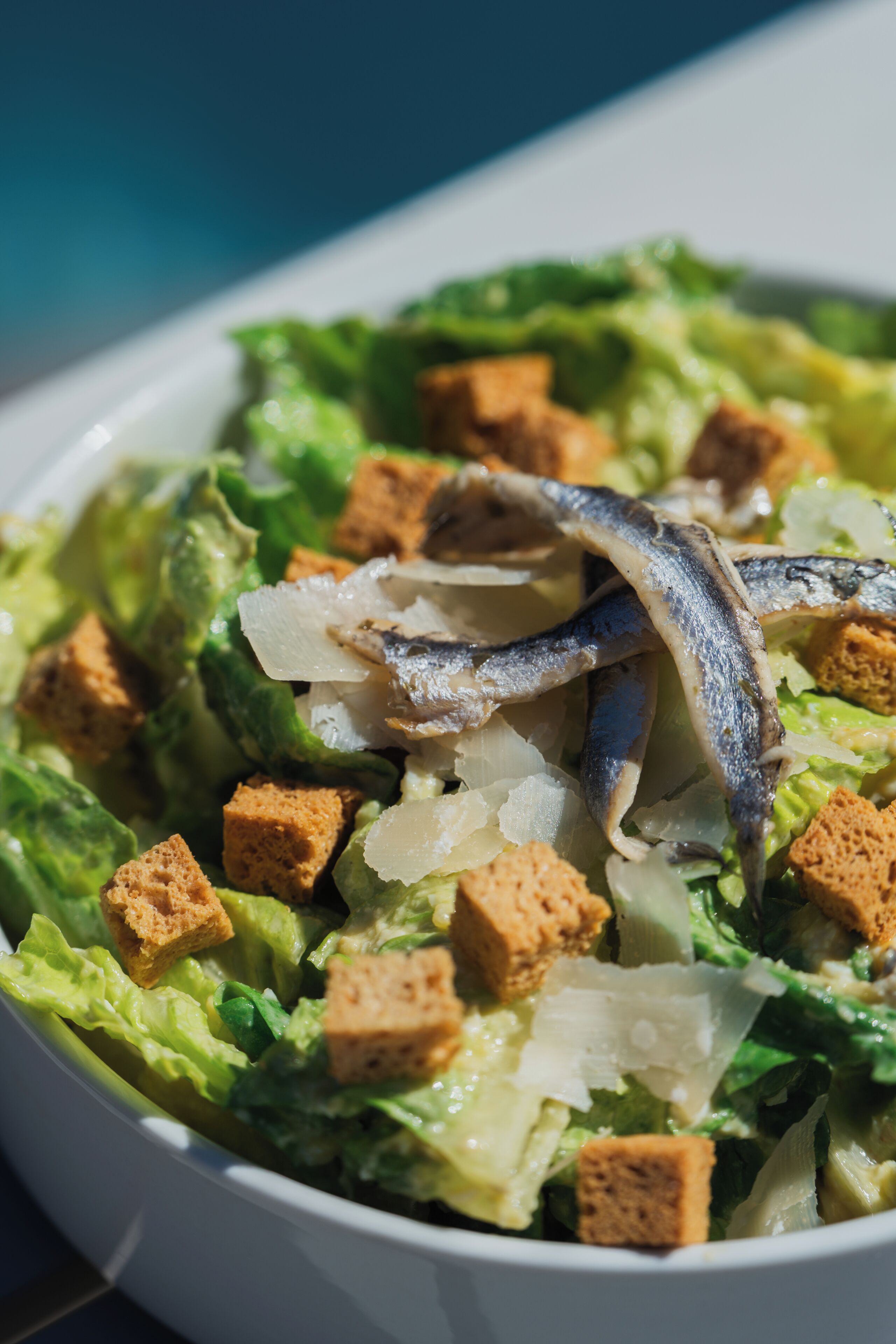 A bowl of salad with lettuce, croutons, and fish.