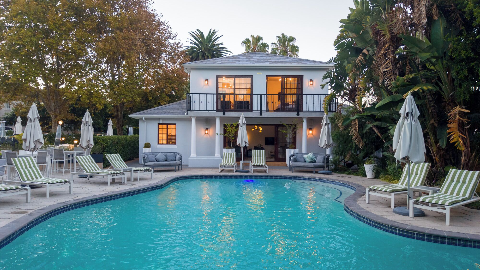 Une maison à deux étages avec une piscine, un espace salon extérieur et des palmiers.