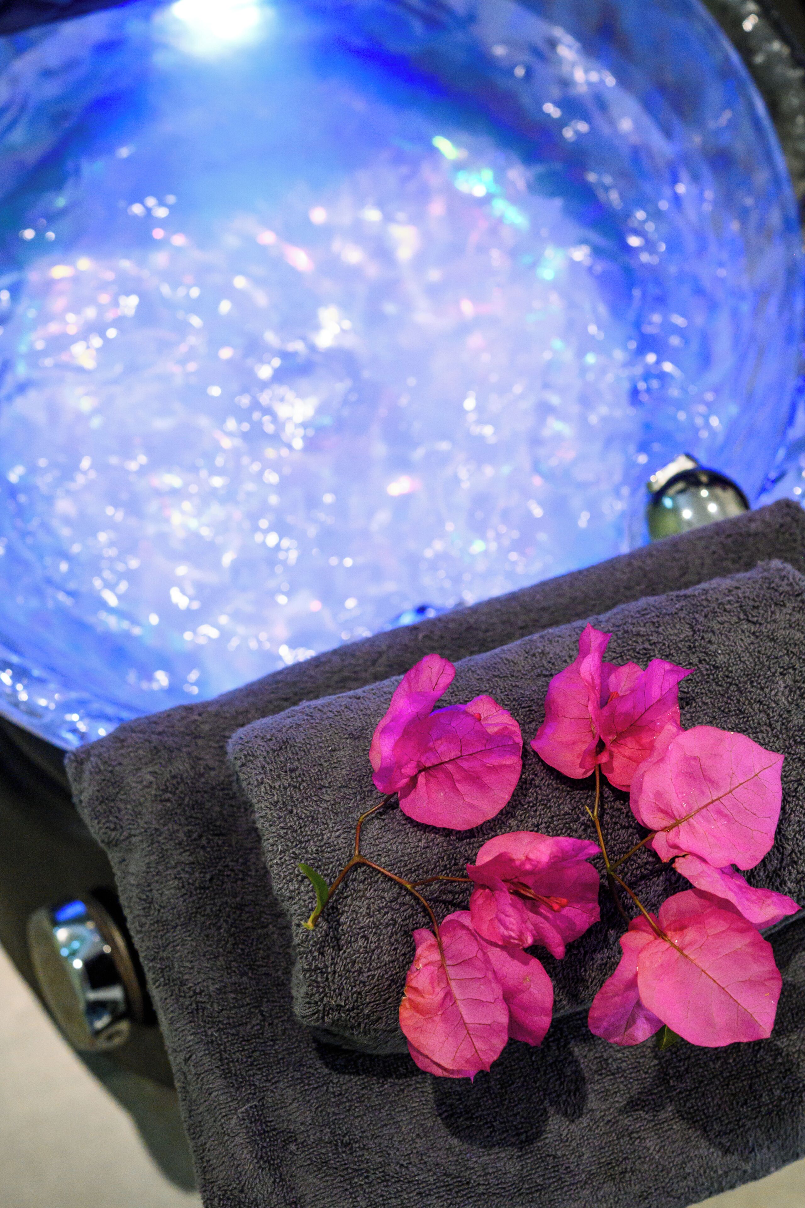 A bathtub with a blue, reflective surface and a towel with pink flowers.