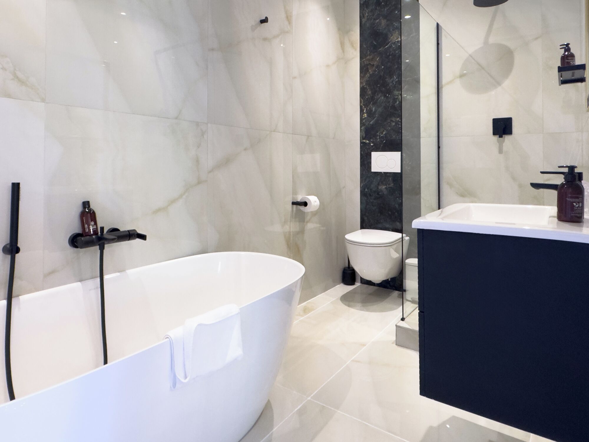 A modern bathroom with a freestanding bathtub, a toilet, and a sink with a dark countertop.