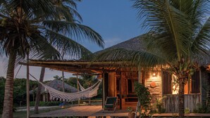 A wooden structure with a thatched roof, surrounded by palm trees and a hammock. - Rancho do Peixe (Cruz)