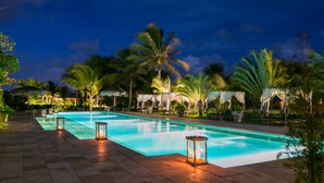 A nighttime swimming pool area with a clear pool, palm trees, and ambient lighting. - Rancho do Peixe (Cruz)