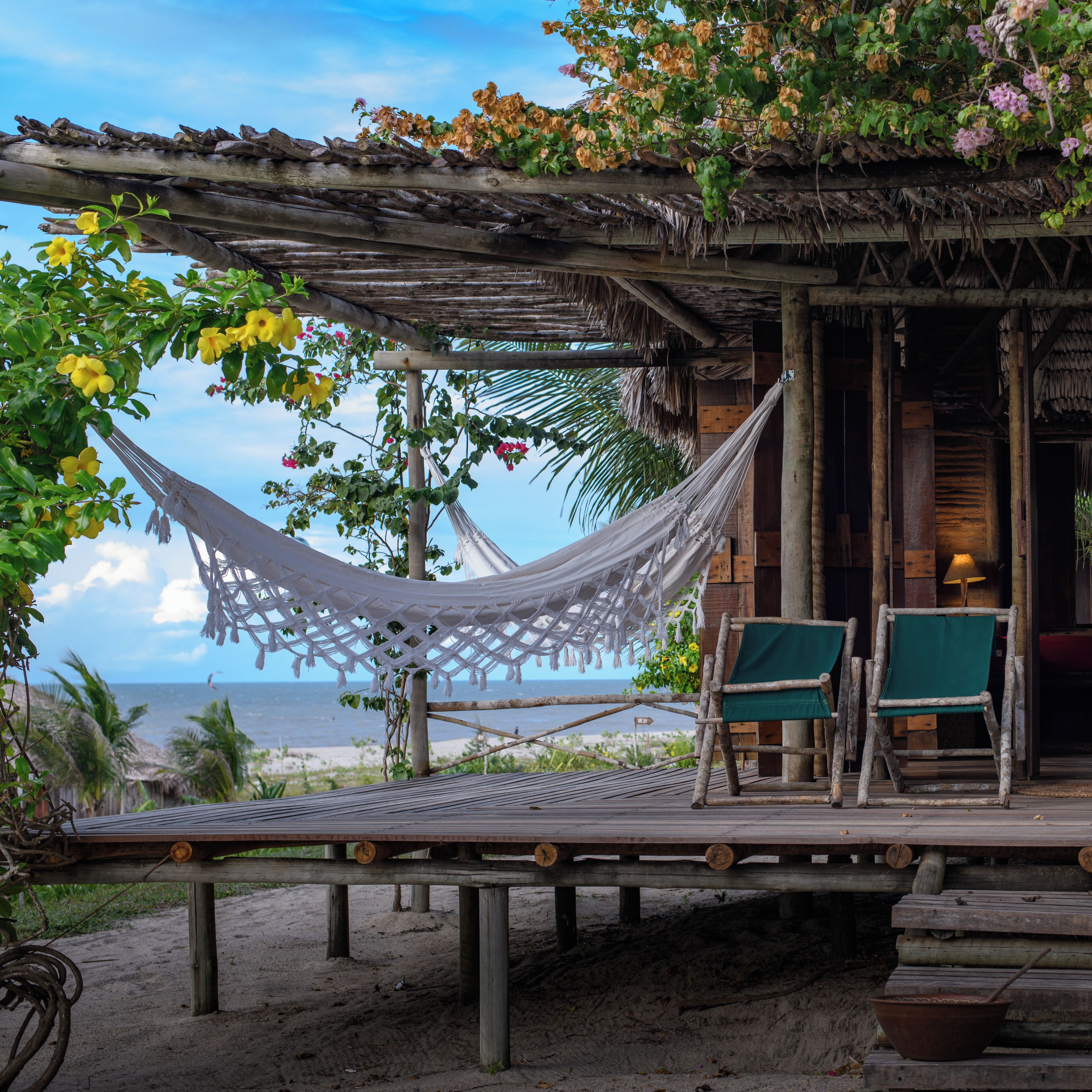 Een hangmat, twee groene stoelen, een houten terras en uitzicht op de oceaan.