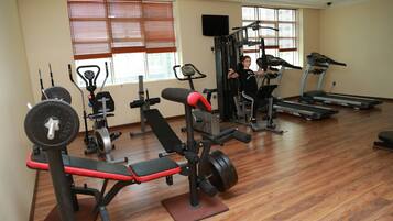 Une salle de sport équipée de divers appareils d’exercice, notamment des tapis de course, un banc de développé couché et des appareils de musculation.