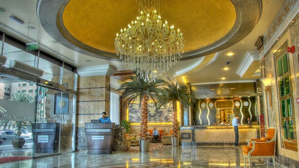A hotel lobby with a grand chandelier, palm trees, and a reception desk. - Sharjah Palace Hotel (Sharjah)