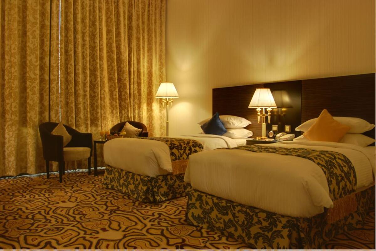 Een hotelkamer met twee bedden, een stoel, een tafeltje en een lamp.
