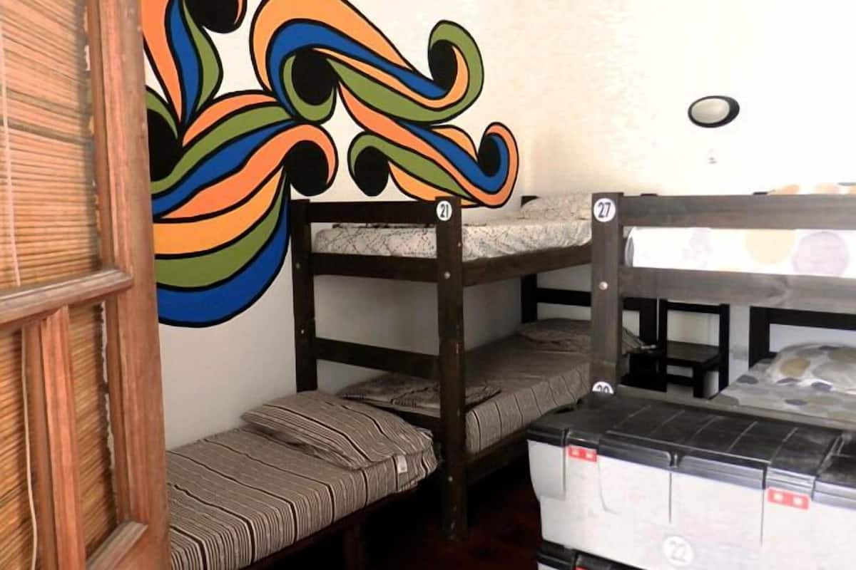 Ein Stockbett mit Matratze und Kissen, eine Holztür und eine Wand mit einem farbenfrohen, abstrakten Muster.
