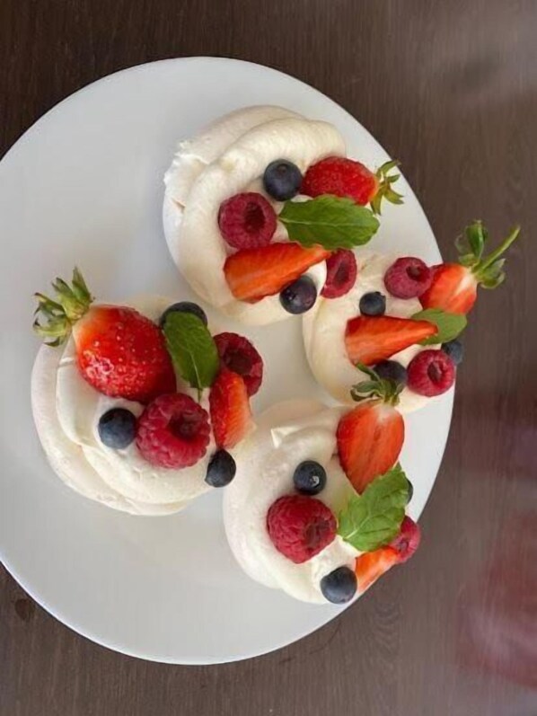 Un plato con tres postres de merengue coronados con fresas, frambuesas, arándanos y hojas de menta.