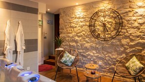 A spa area with a hot tub, wicker chairs, a stone wall, and a clock.