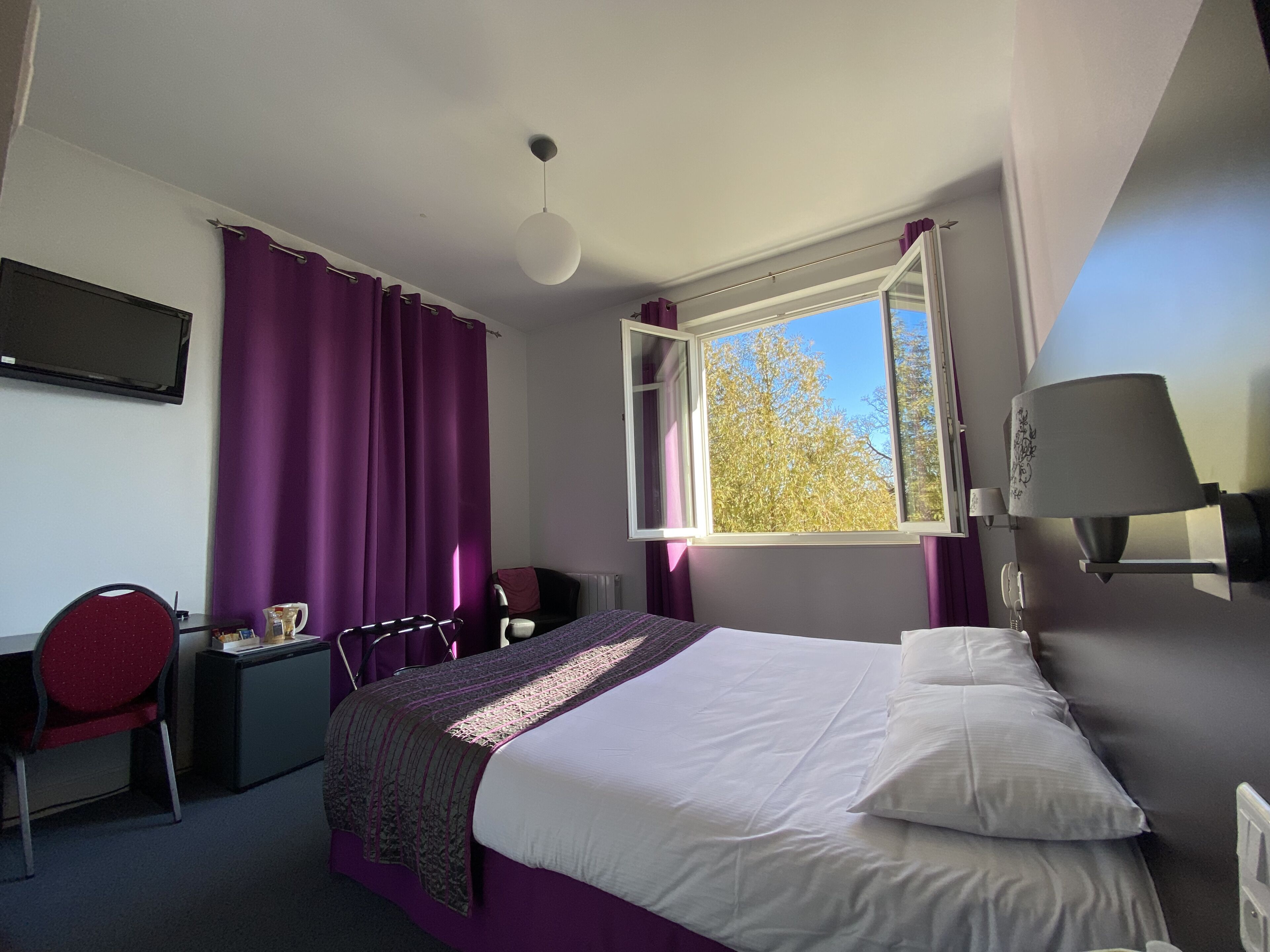 Une chambre à coucher avec un lit, un bureau, une chaise et une fenêtre avec des rideaux.