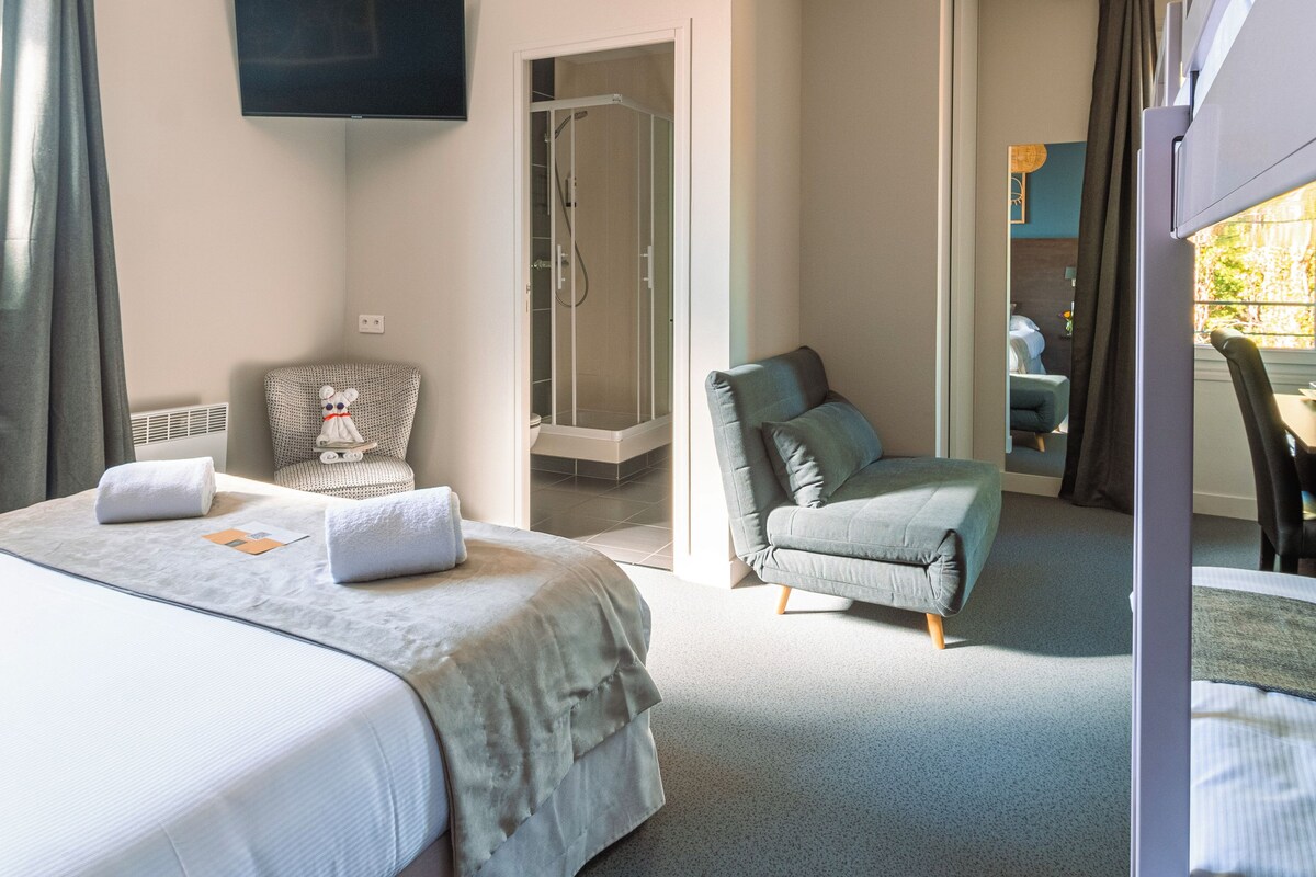 A hotel room with a bed, a chair, a TV, and a shower area.