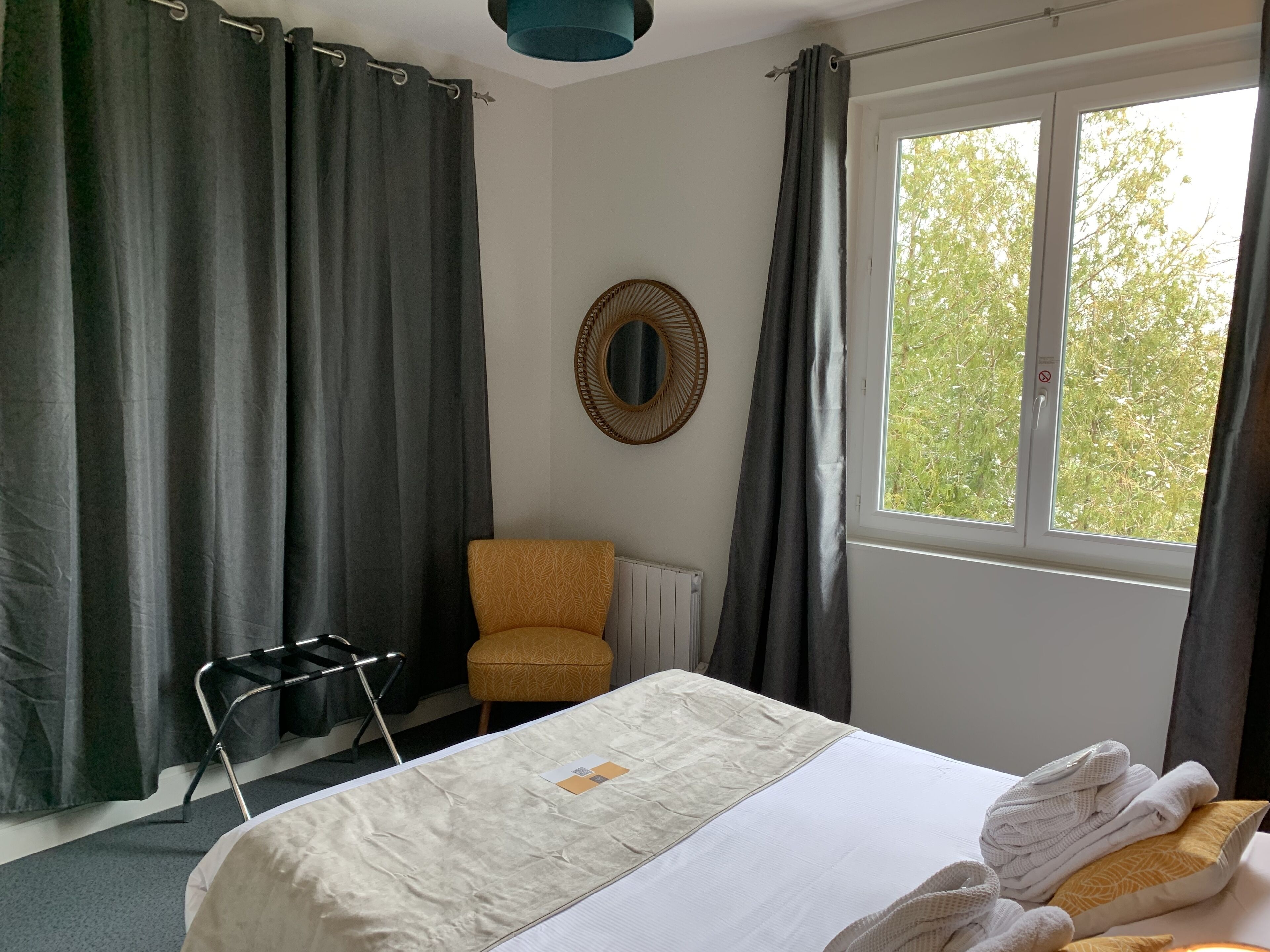 A hotel room with a bed, a chair, a window with curtains, and a radiator.