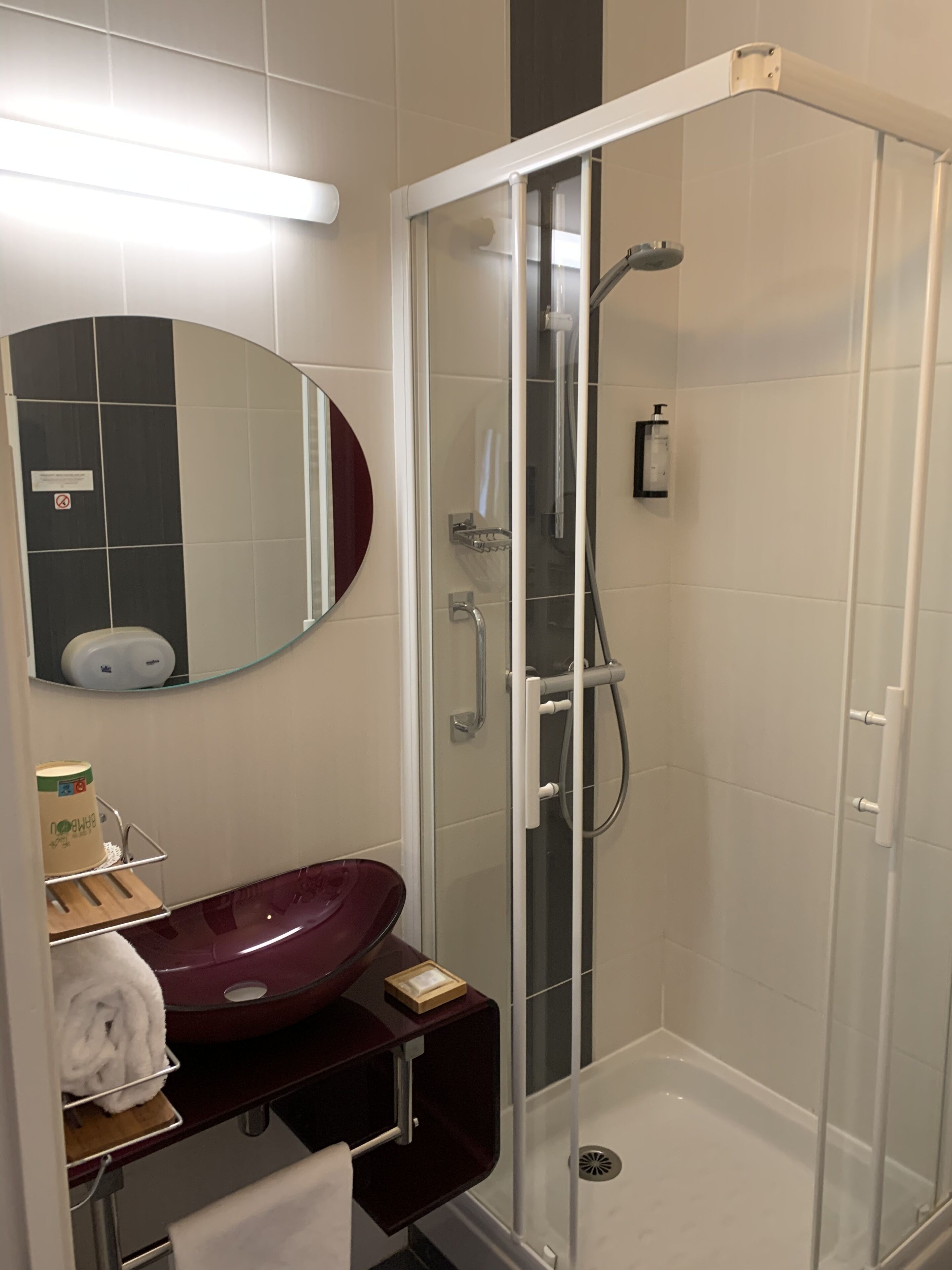 Un baño moderno con ducha envuelta en vidrio, un espejo redondo y un lavamanos de mármol.