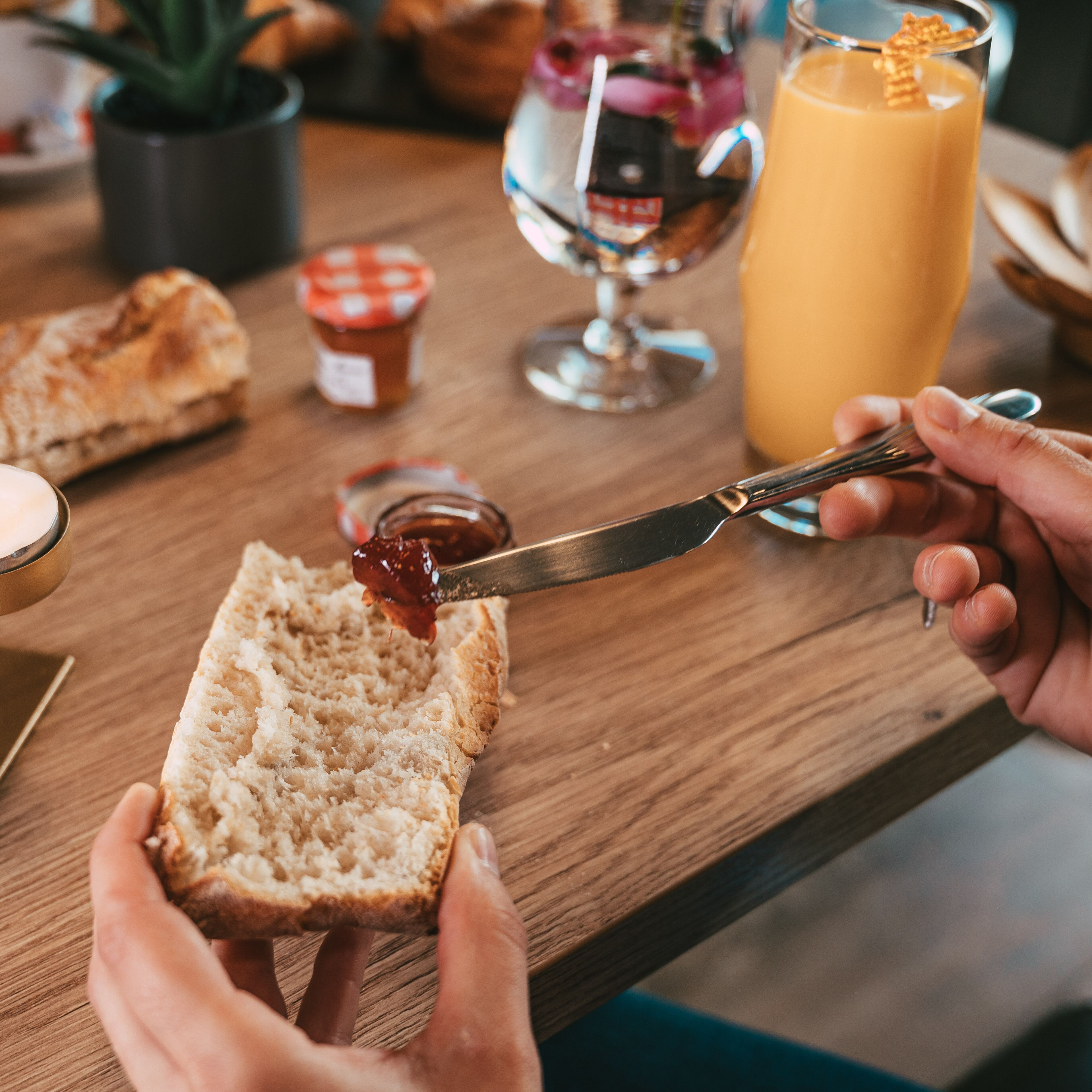 Una persona untando mermelada sobre una rebanada de pan sobre una mesa de madera.