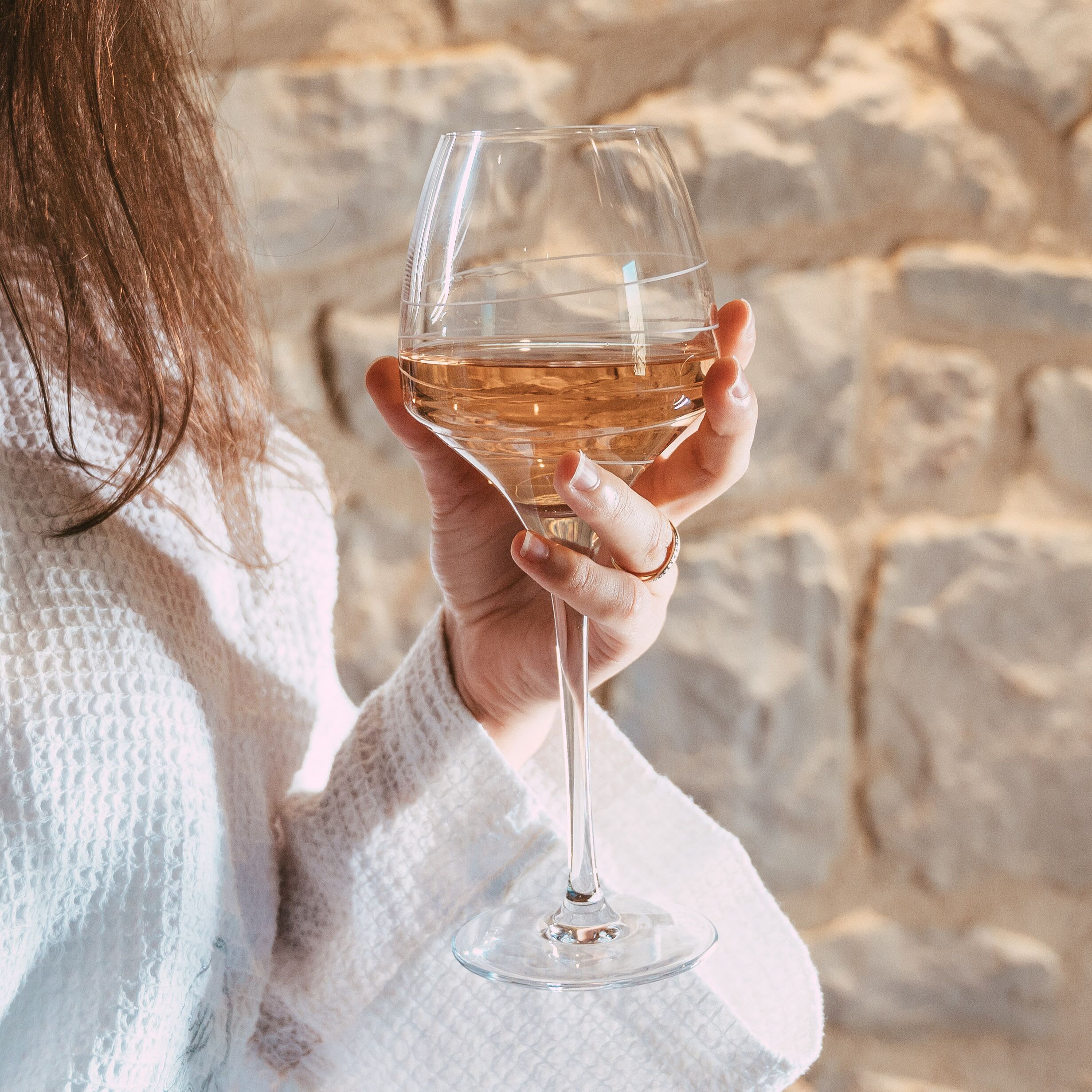 A person holding a wine glass with a stone wall background.