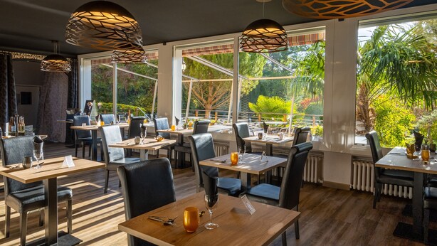 A restaurant with wooden tables and chairs, large windows, and hanging pendant lights.