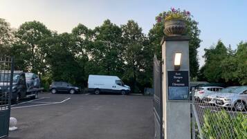 A parking lot with a white van and a car, surrounded by trees and a metal fence.