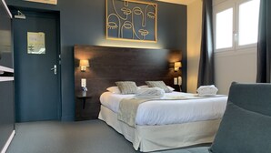 A hotel room with a large bed, two bedside lamps, a headboard, a grey armchair, and a wall art piece.