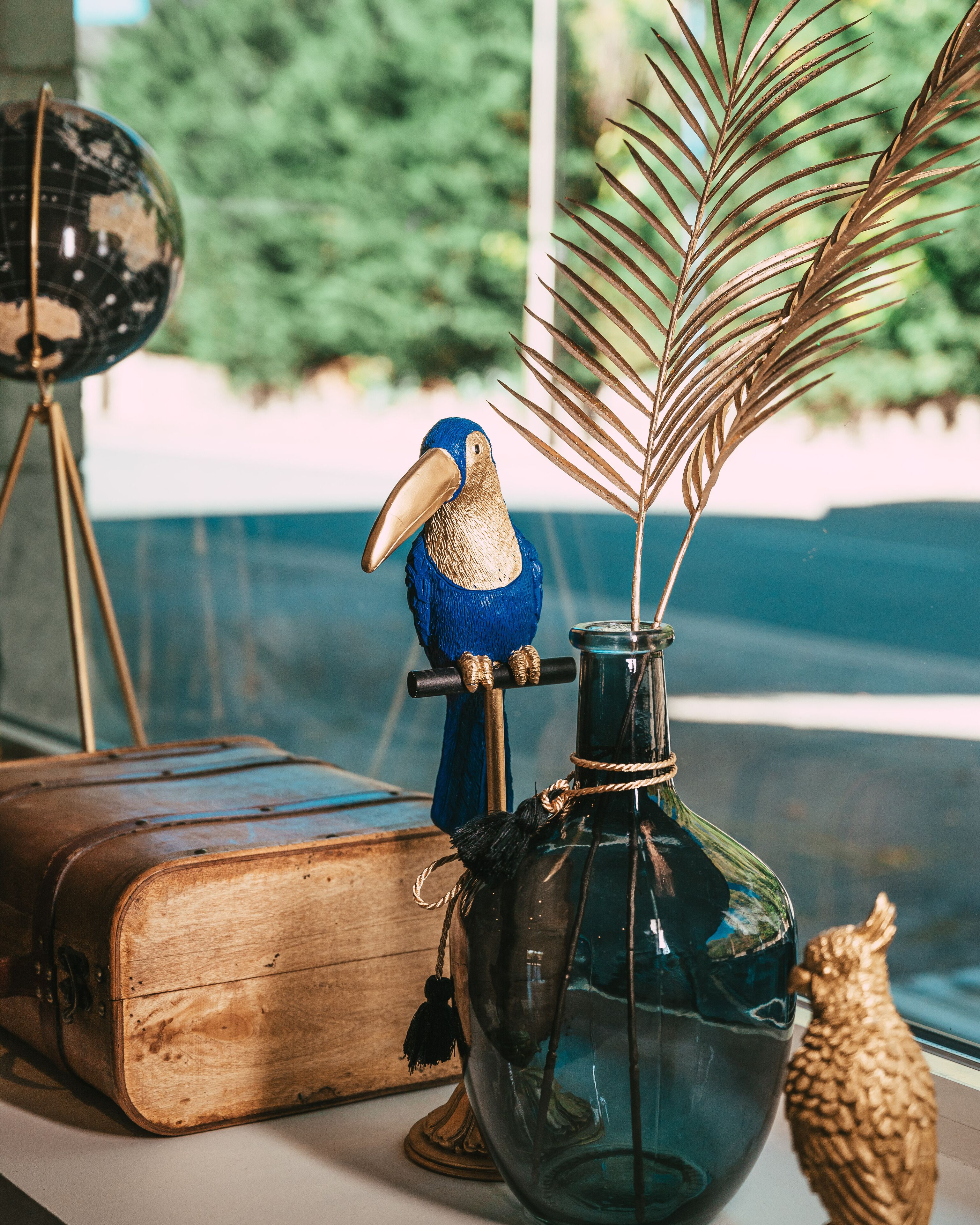 A vintage-style room with a globe, a blue parrot figurine, a glass vase with a feather, and a wooden book.