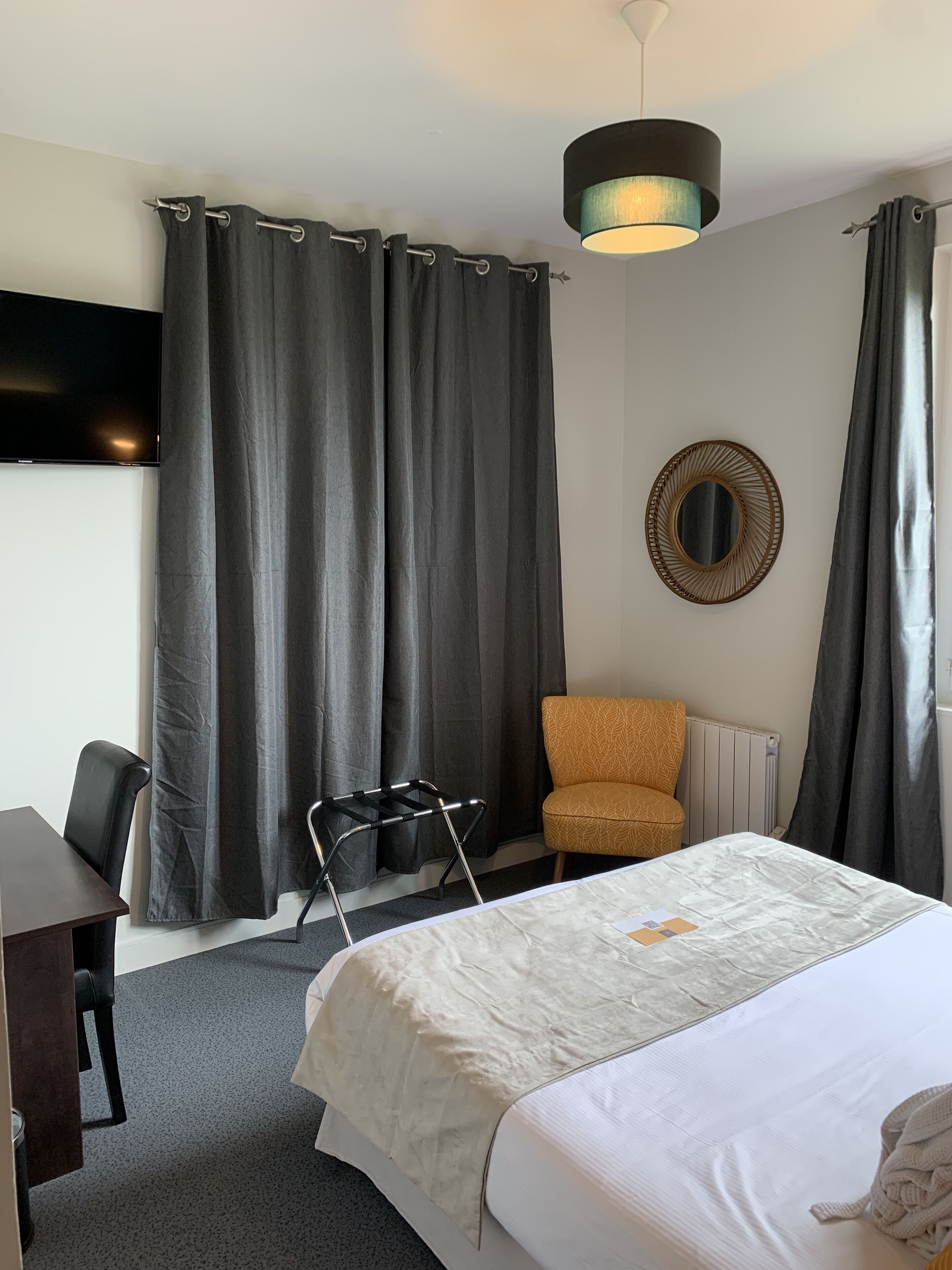 A hotel room with a bed, a desk, a chair, a TV, and a mirror.