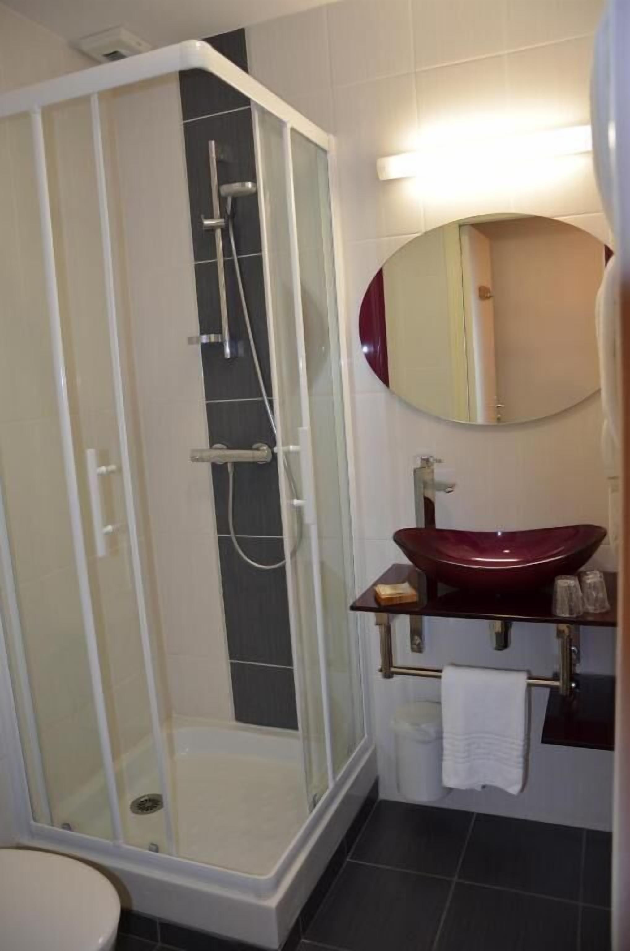 A modern bathroom with a glass-enclosed shower, a round mirror, and a dark-toned sink.
