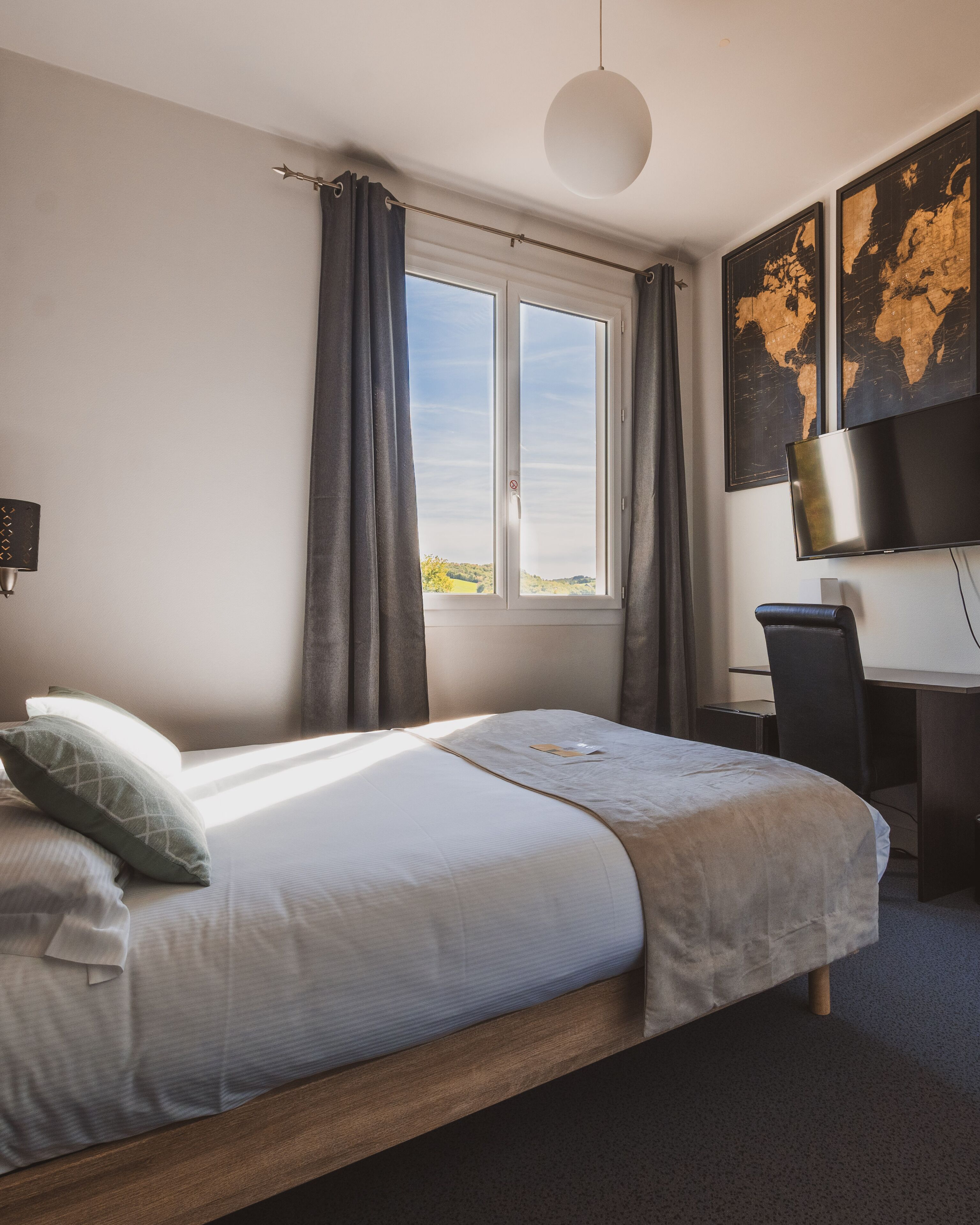 A hotel room with a bed, a desk, a chair, a TV, and a window with curtains.