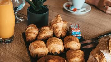 Une table en bois avec des croissants, un verre de jus d’orange, une tasse de café et une petite plante en pot.