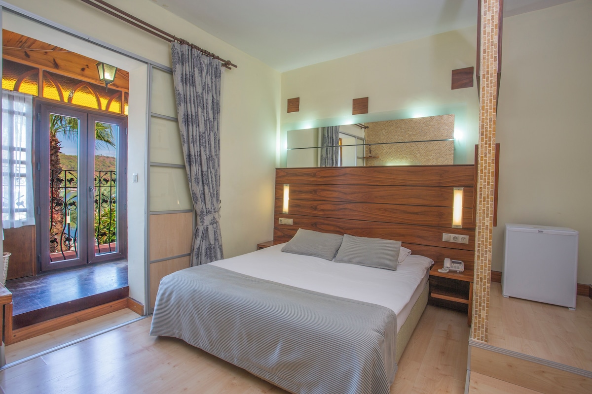 Un dormitorio con cama, mesitas de noche, espejo, un refrigerador pequeño y vistas a través de una ventana.