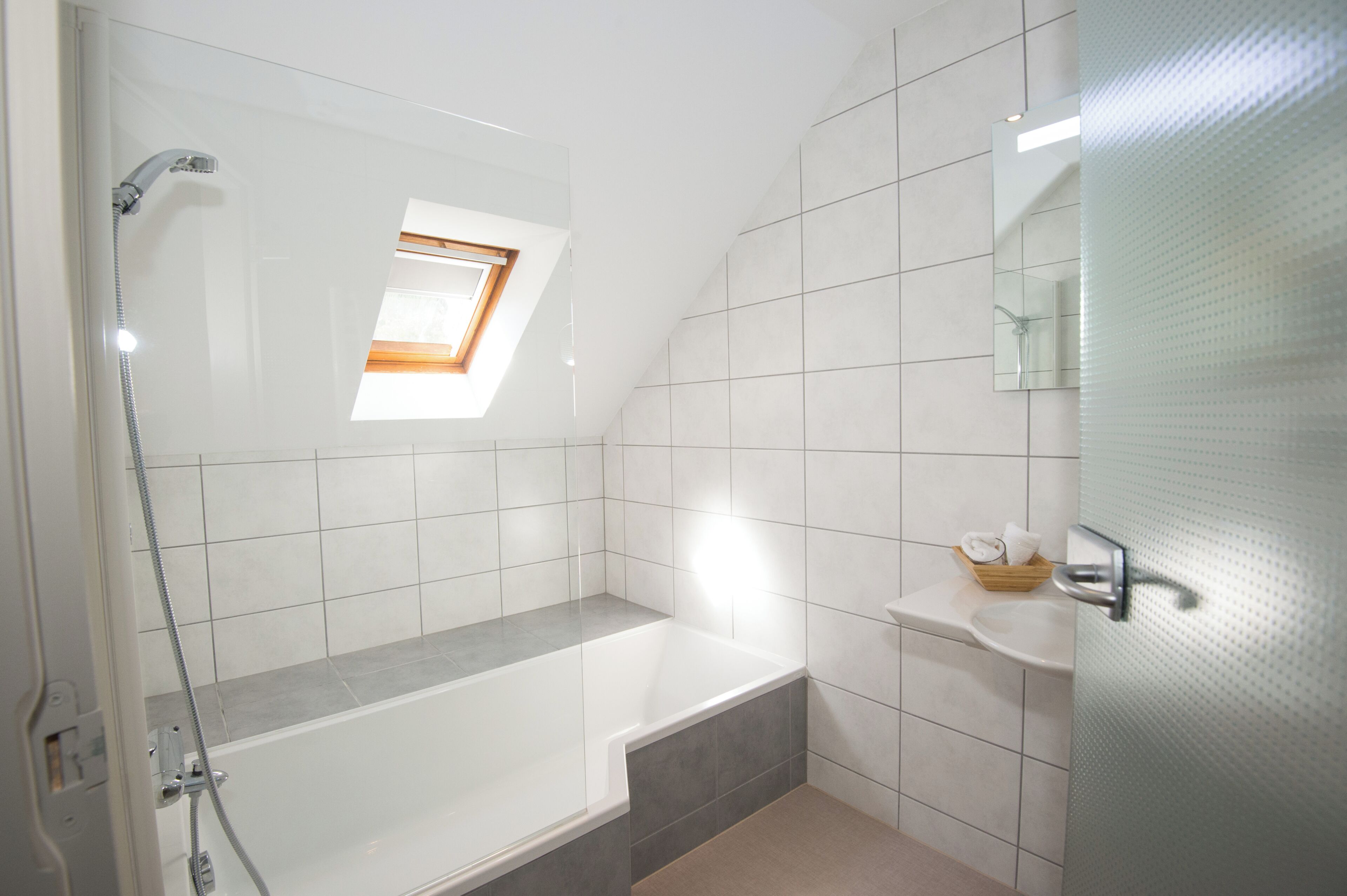 A modern bathroom with a shower, a bathtub, a small window, and a sink with a towel and soap.
