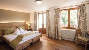 A bedroom with a wooden bed, a chair, a window with curtains, and a radiator. - Logis Hôtel-Restaurant Auberge du Mehrbachel (Saint-Amarin)