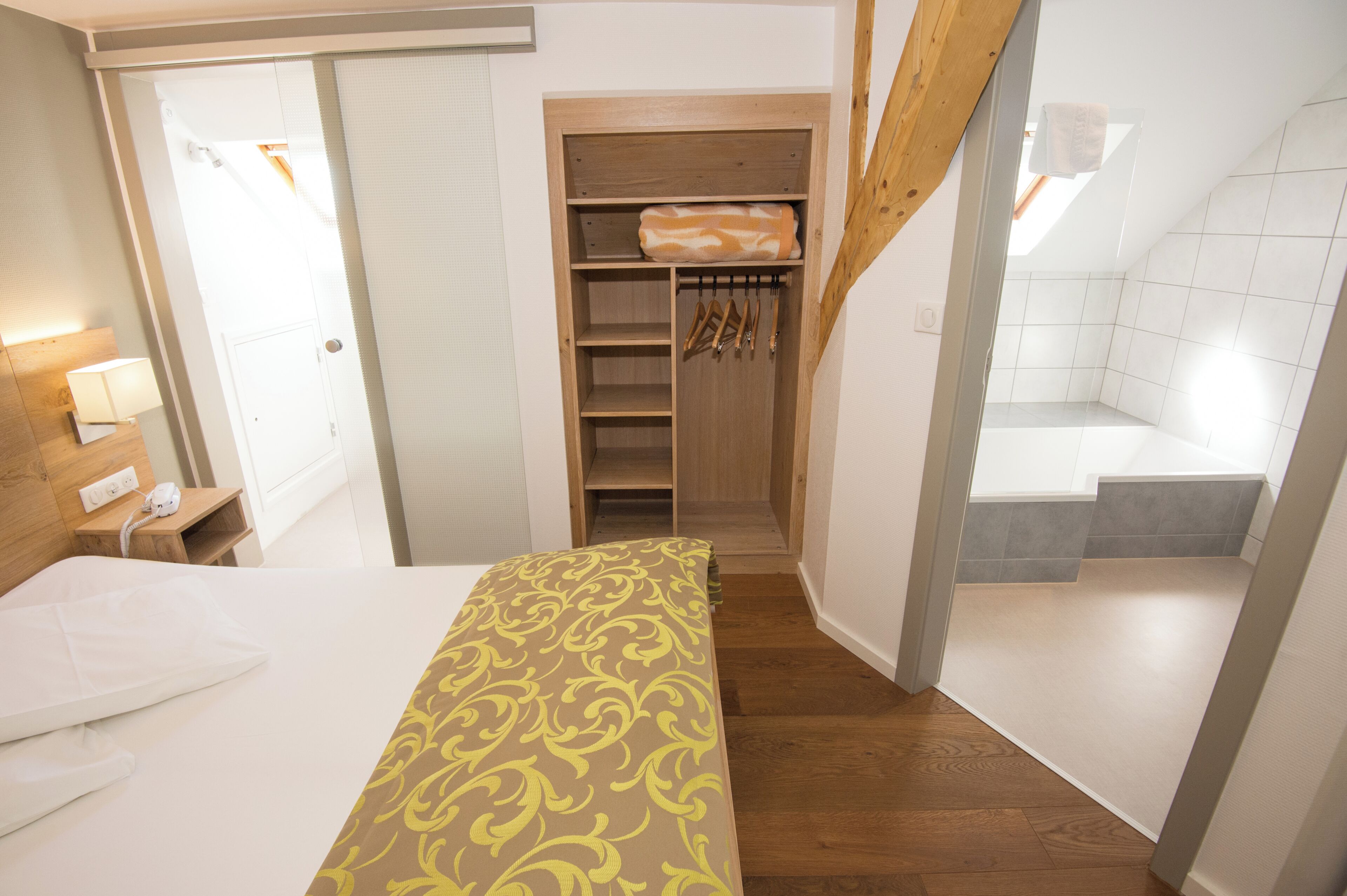 A hotel room with a bed, a wooden closet, a bathroom with a shower, and a staircase.