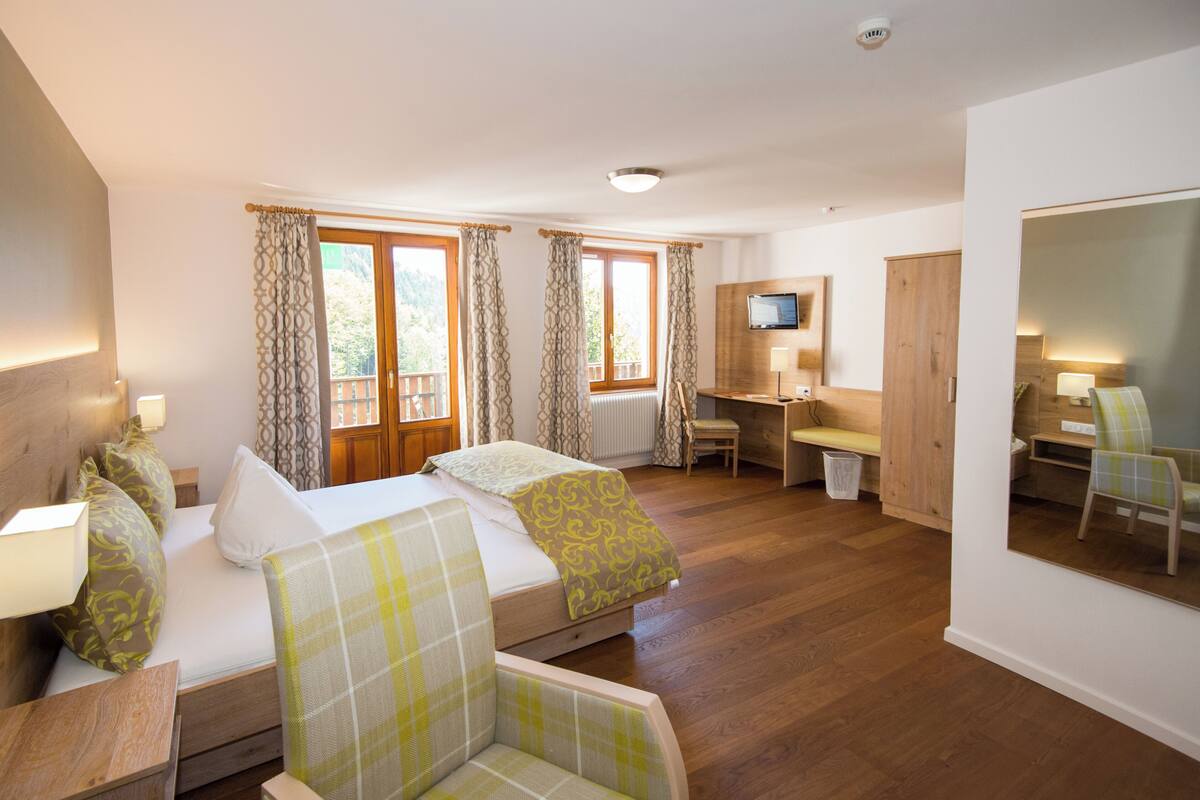 Habitación de hotel con cama, dos sillas, escritorio, televisor y ventana con cortinas.