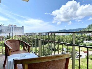 A balcony with a table and chair, overlooking a cityscape with buildings and a road.