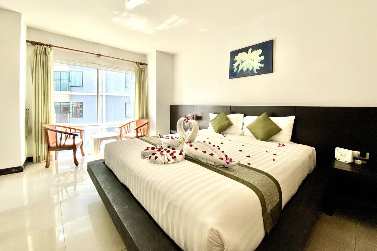 A hotel room with a large bed, a chair, a small table, and a window with curtains.