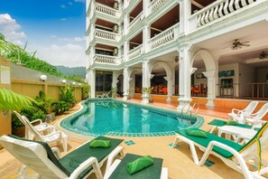 A pool area with lounge chairs and a view of a multi-story building with balconies.