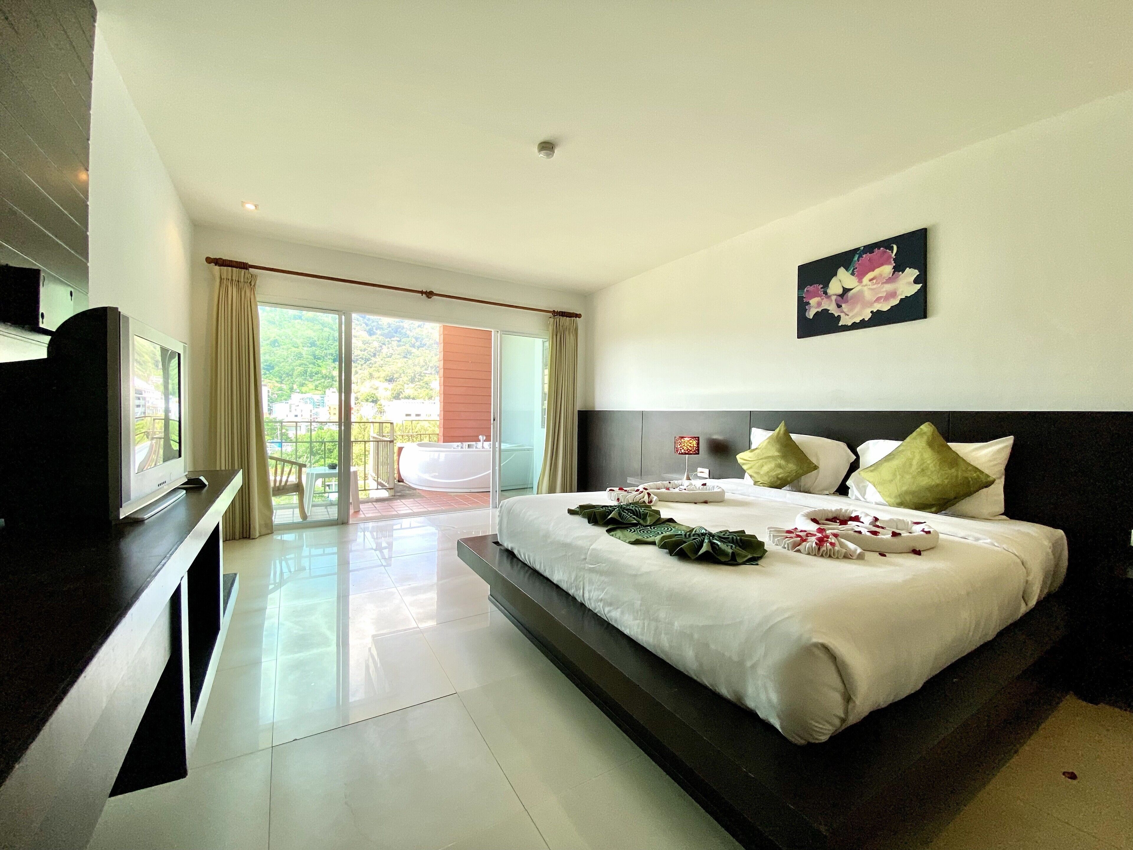 Habitación de hotel con una cama grande, un televisor en un soporte, un balcón con vistas a zonas verdes y un cuadro en la pared.