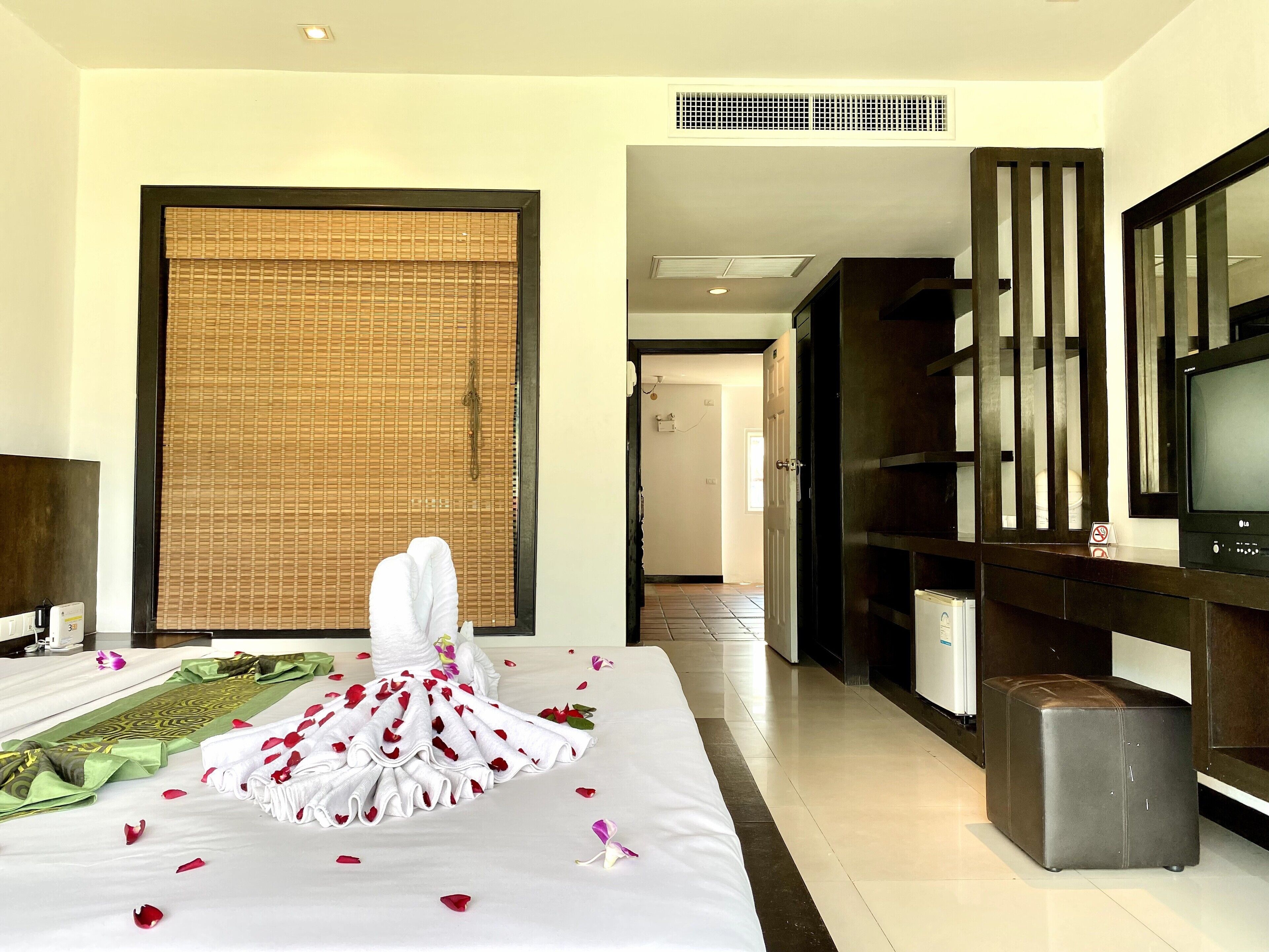 Habitación de hotel con cama, televisor, ventana grande con persiana de bambú y puerta que da a otra habitación.