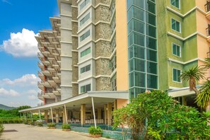 A multi-story hotel with a covered entrance, balconies, and a view of greenery.